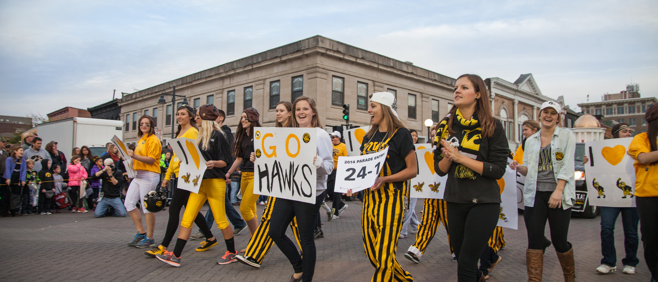 Students walking in the homecoming parade with a sign that says "Go Hawks!"